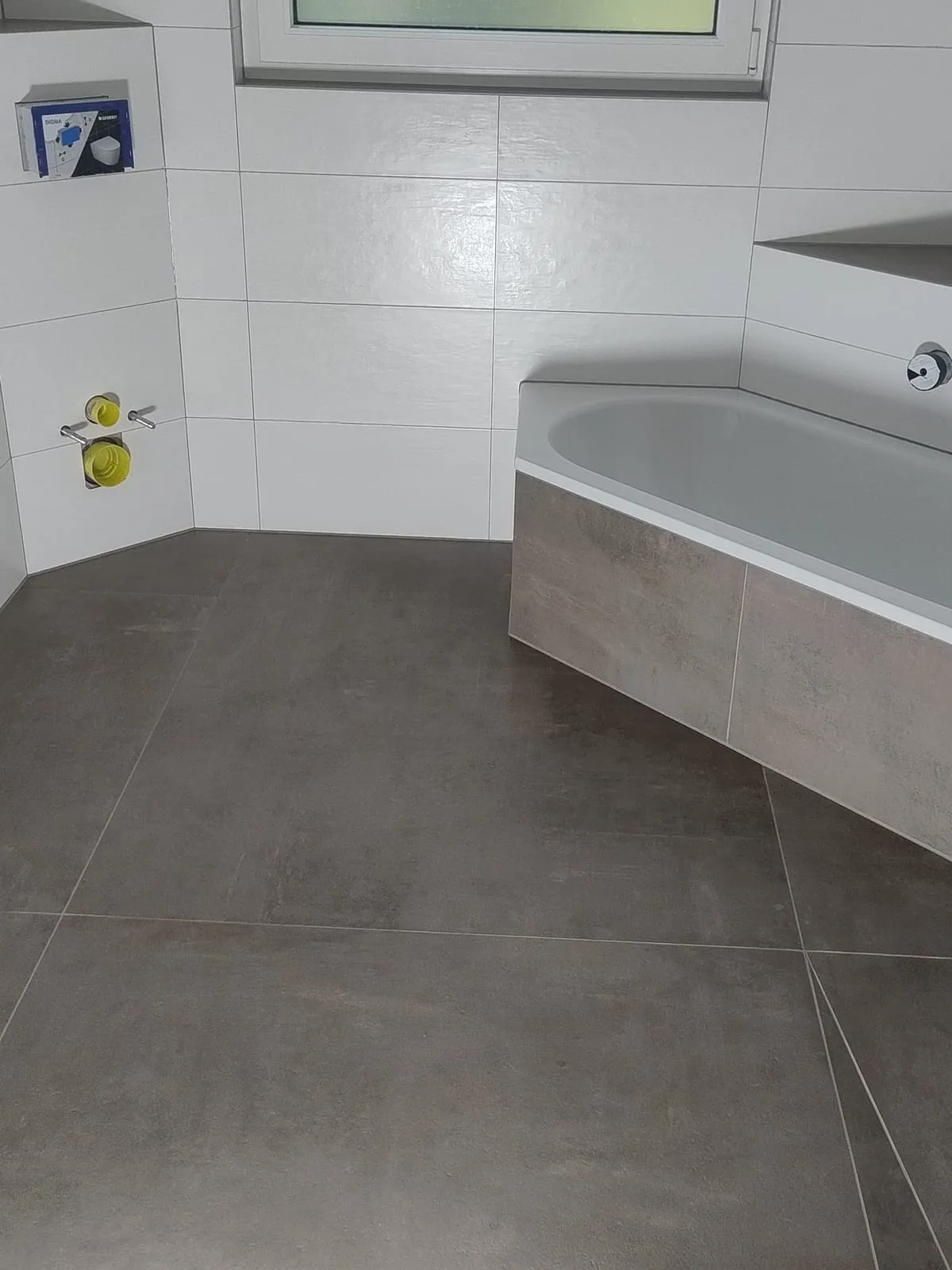 Diagonal verlegte Großformatplatten in Graubraun, rechts die eingeflieste Badewanne