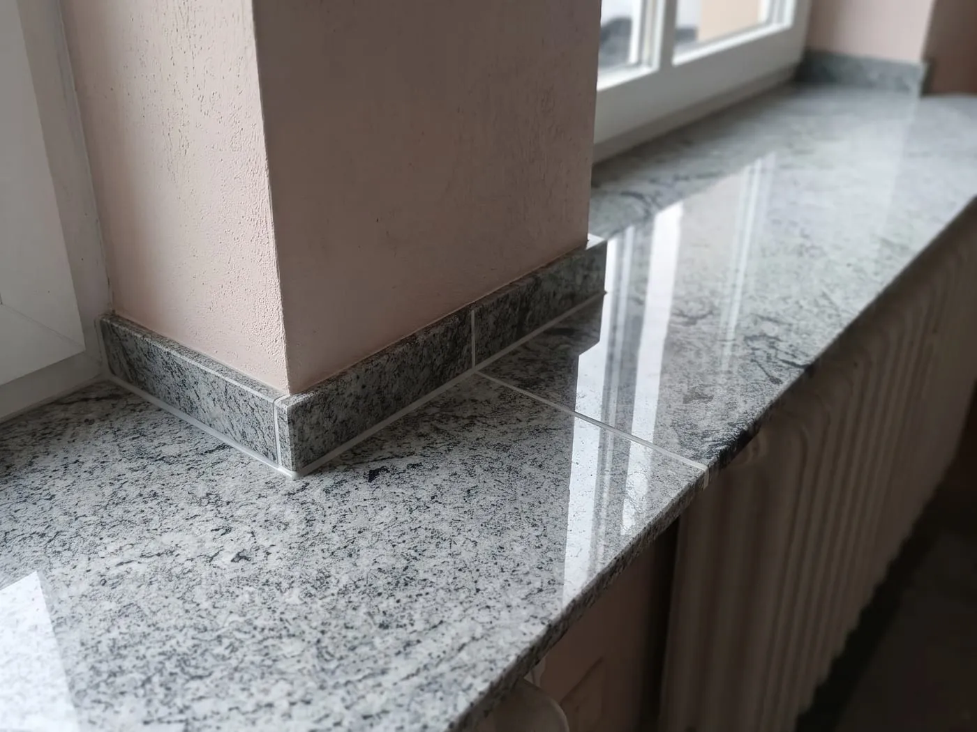 Zwei polierte Innenfensterbänke aus hellem Granit laufen um einen Mauerpfeiler, dessen Sockel passend mit Granitleisten eingefasst ist