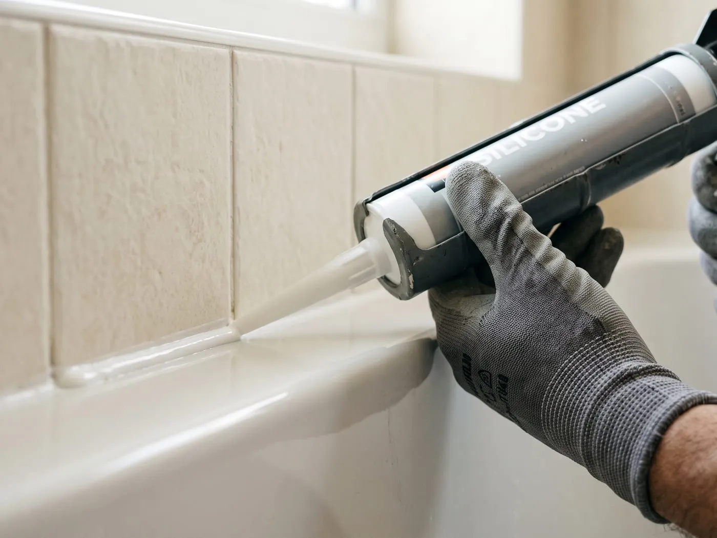 Silikonfuge wird mit der Kartuschenpistole am Rand einer Badewanne gezogen