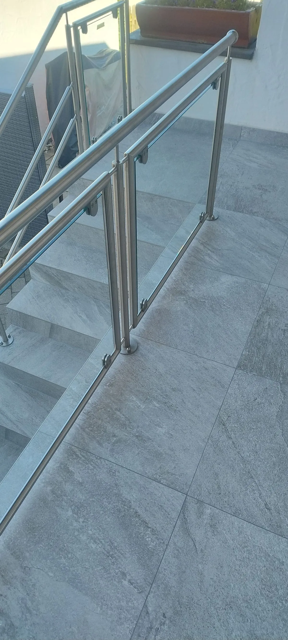 Detail des Edelstahl-Glasgeländers auf Platten in Gneis-Optik am Übergang von Treppe und Terrasse