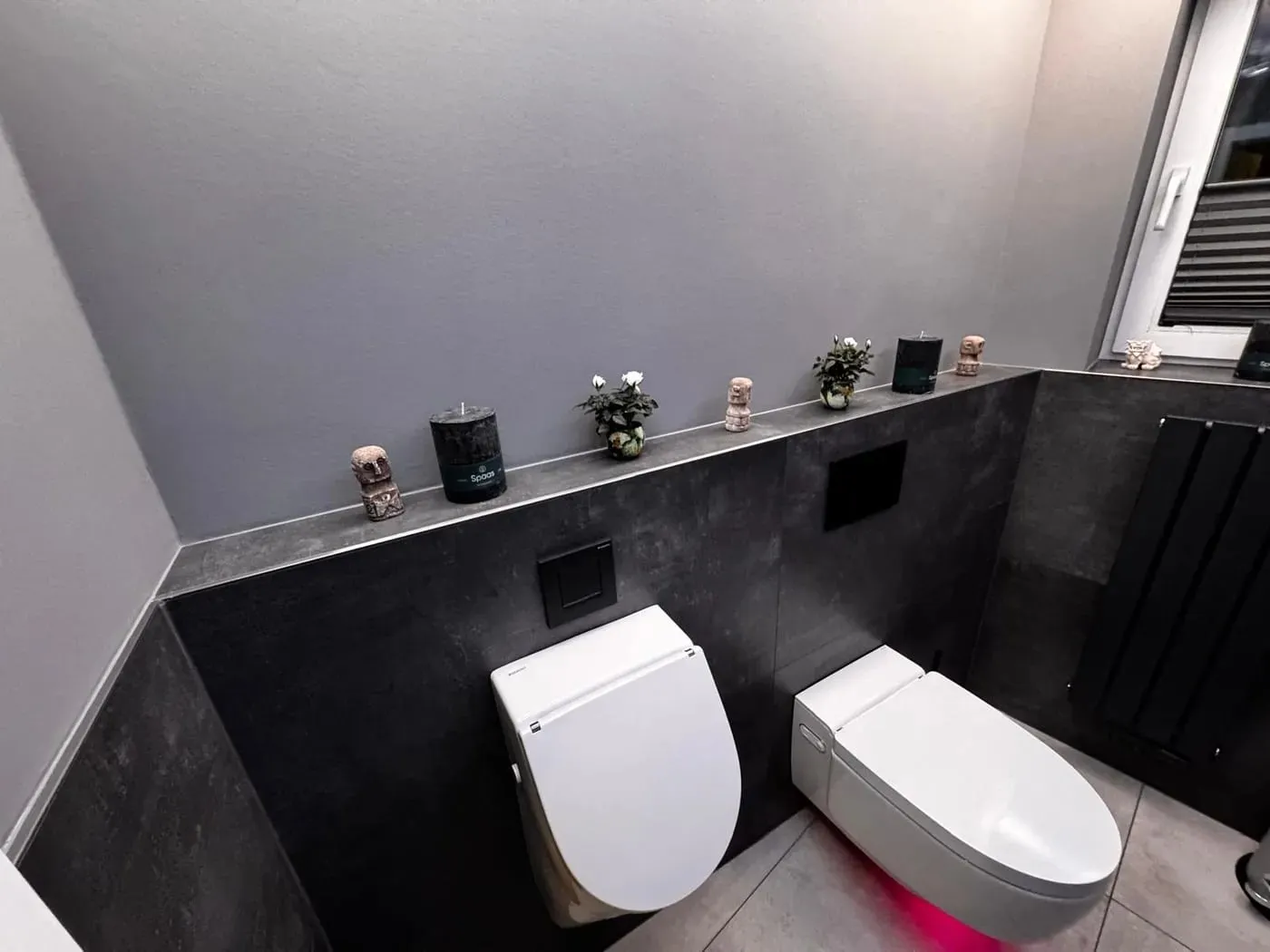 Gäste-WC nach dem Umbau: dunkle Wandplatten in Betonoptik mit umlaufender Ablage, Urinal und Dusch-WC
