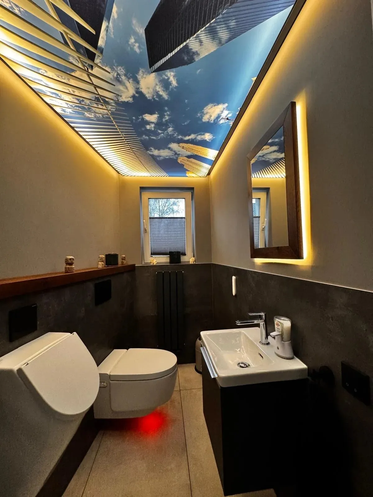 Das Gäste-WC nach dem Umbau: dunkle Betonoptik-Wände, beleuchtete Himmeldecke, neues Dusch-WC und Urinal