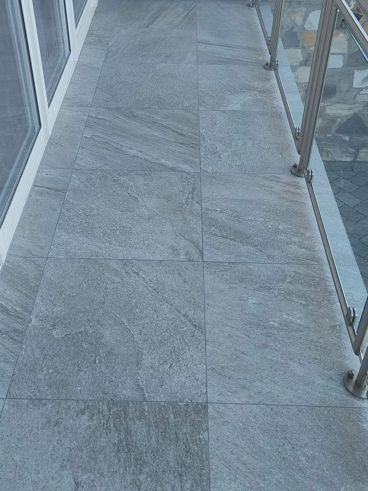 Neu belegte Terrassenfläche mit Platten in Gneis-Optik, rechts das Edelstahl-Glasgeländer