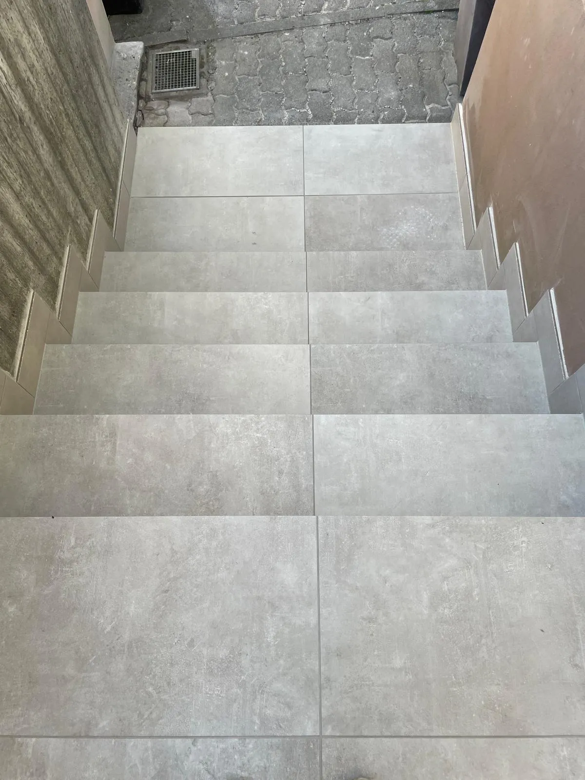 Blick vom Podest die fertige Treppe hinab: die Plattenteilung läuft über alle Stufen durch, seitlich schmale Wangenstreifen