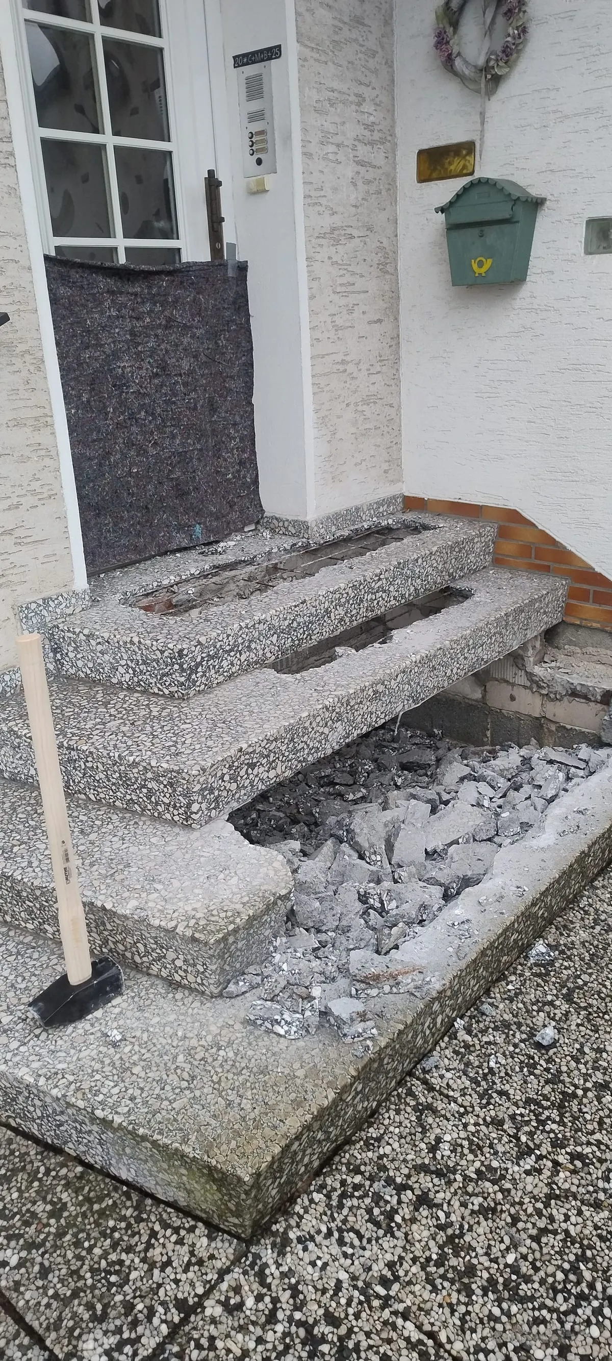 Abbruch der alten Treppe: aufgestemmte Waschbetonstufen mit freigelegter Bewehrung, davor Bruchmaterial und ein Vorschlaghammer