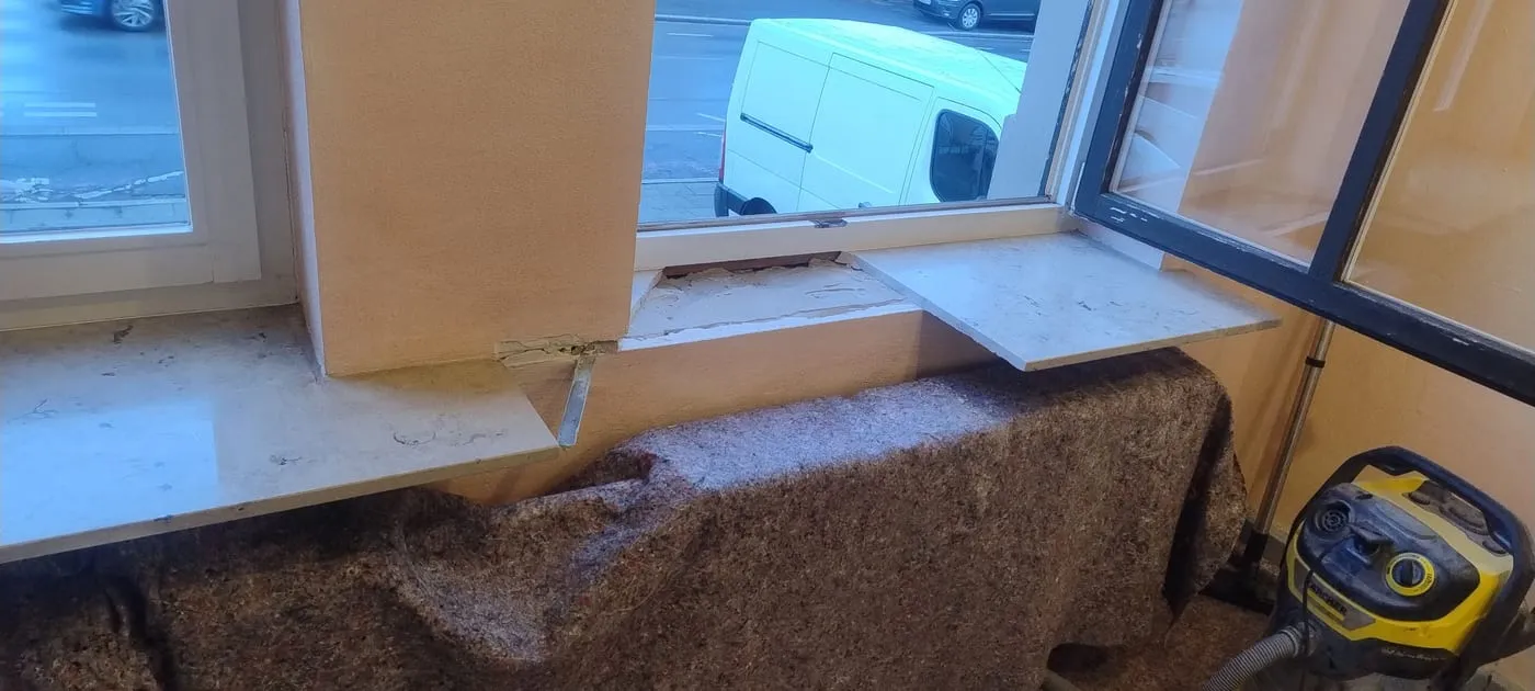 Fensterbrüstung nach der Demontage der alten Fensterbank: offenes Mörtelbett, die neuen Granitplatten liegen zur Anprobe auf, der Heizkörper ist mit Vlies abgedeckt